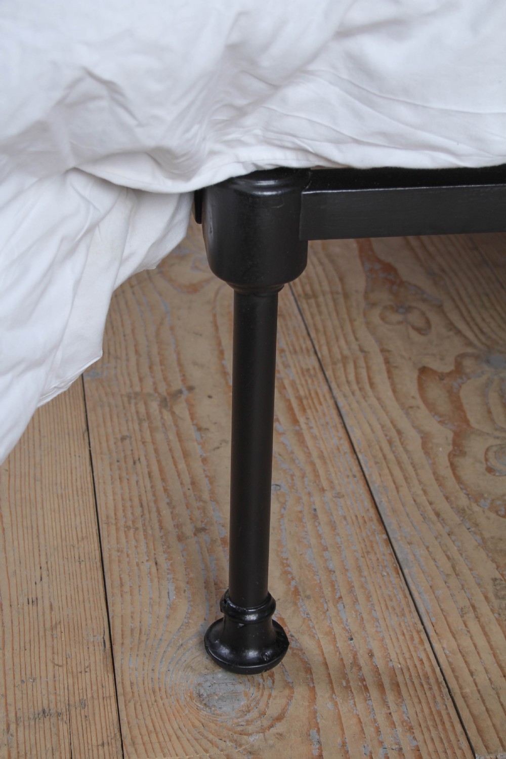 A Victorian single cast iron bedstead with black vertical spindles, brass finials, and white bed linen. View V