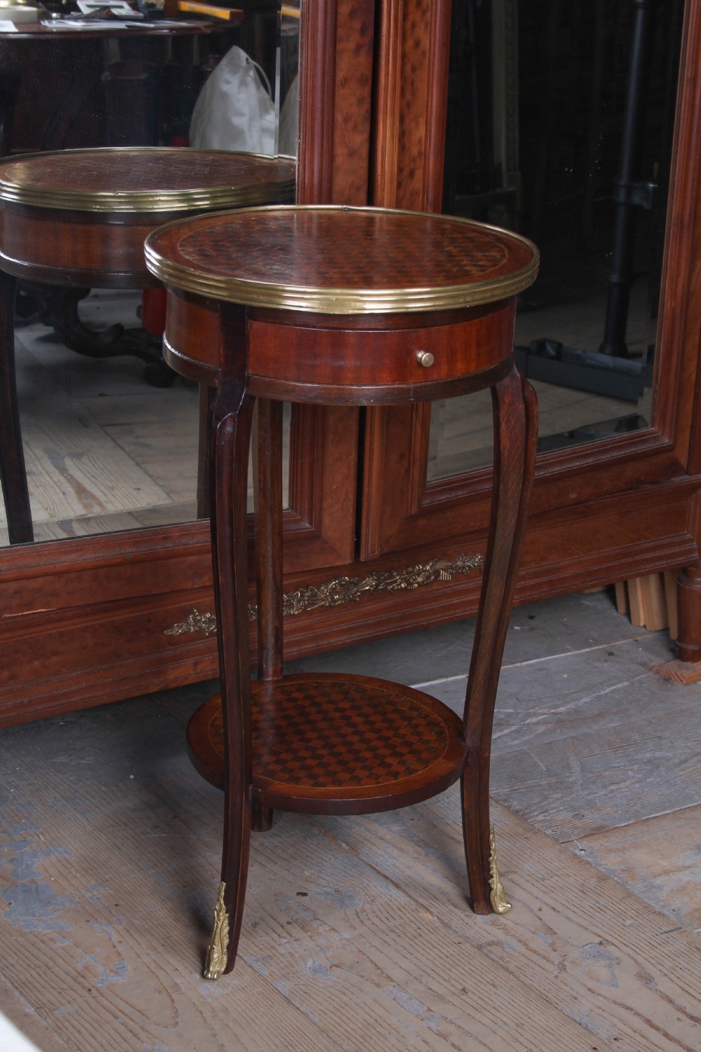 A small, round Louis XV style mahogany side table featuring a brass gallery rim, a single frieze drawer, slender cabriole legs with brass feet, and a lower parquetry shelf.