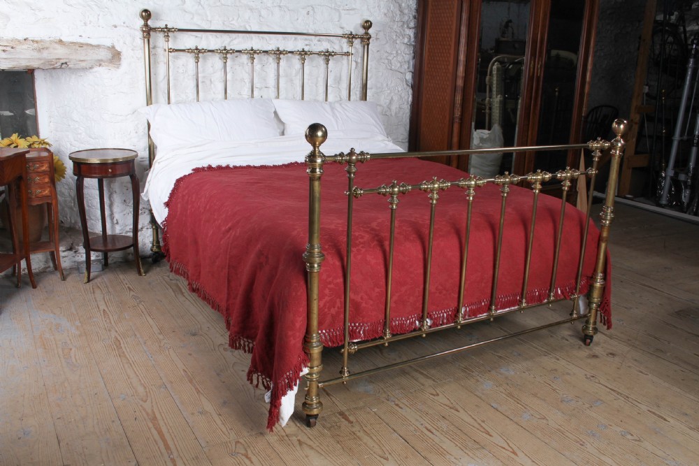 An antique king-sized brass bedstead featuring turned vertical spindles, corner post finials, and a warm aged patina.