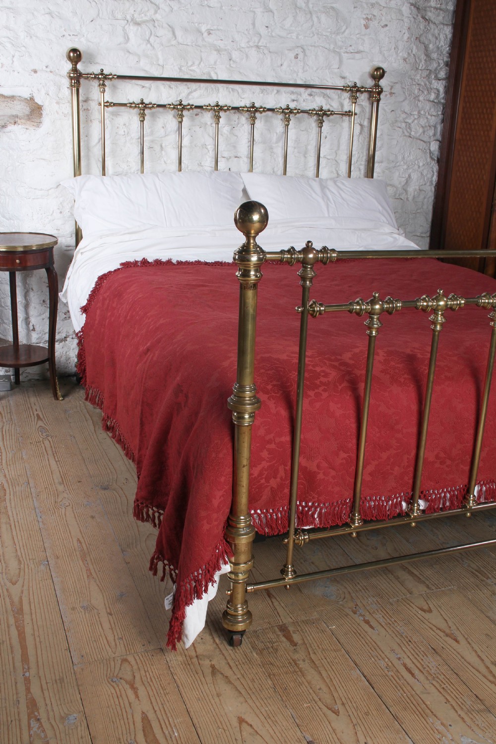 An antique king-sized brass bedstead featuring turned vertical spindles, corner post finials, and a warm aged patina. View II