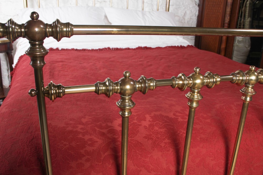 An antique king-sized brass bedstead featuring turned vertical spindles, corner post finials, and a warm aged patina. View V