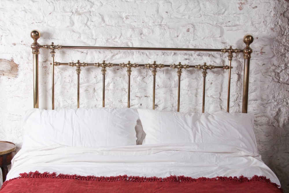 An antique king-sized brass bedstead featuring turned vertical spindles, corner post finials, and a warm aged patina. View VI