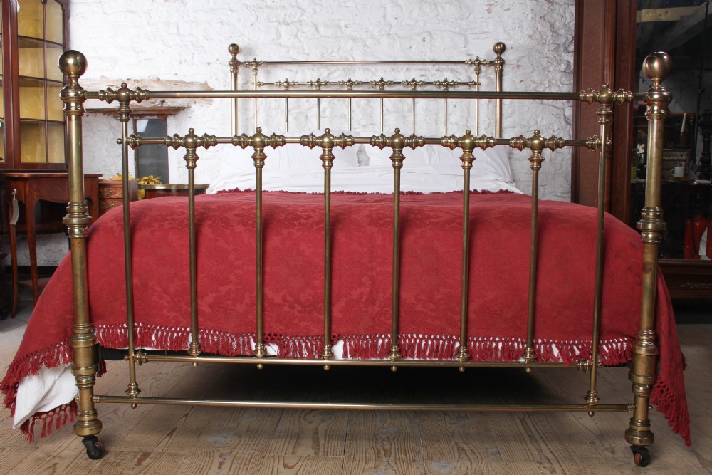 An antique king-sized brass bedstead featuring turned vertical spindles, corner post finials, and a warm aged patina. View VII