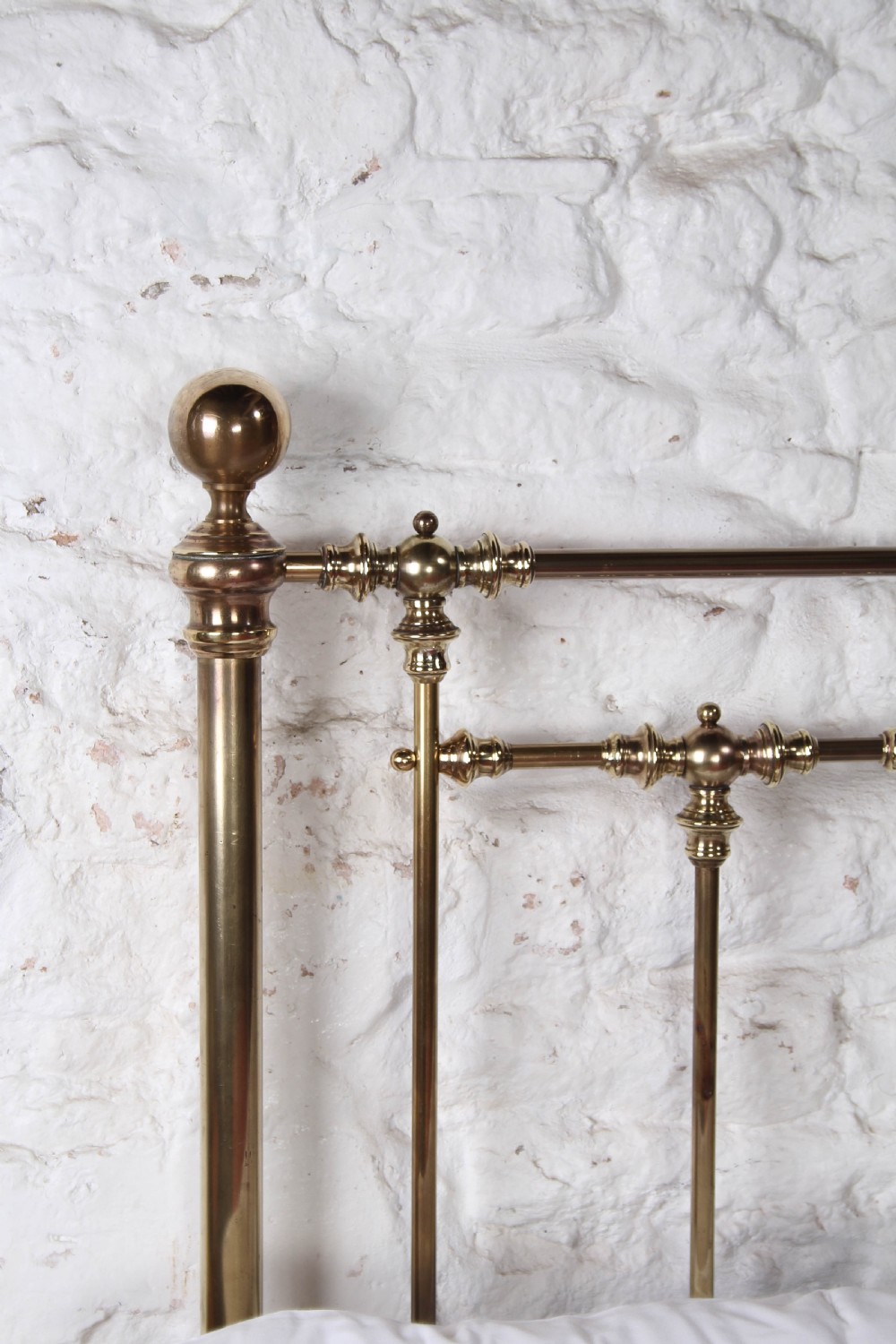 An antique king-sized brass bedstead featuring turned vertical spindles, corner post finials, and a warm aged patina. View VIII