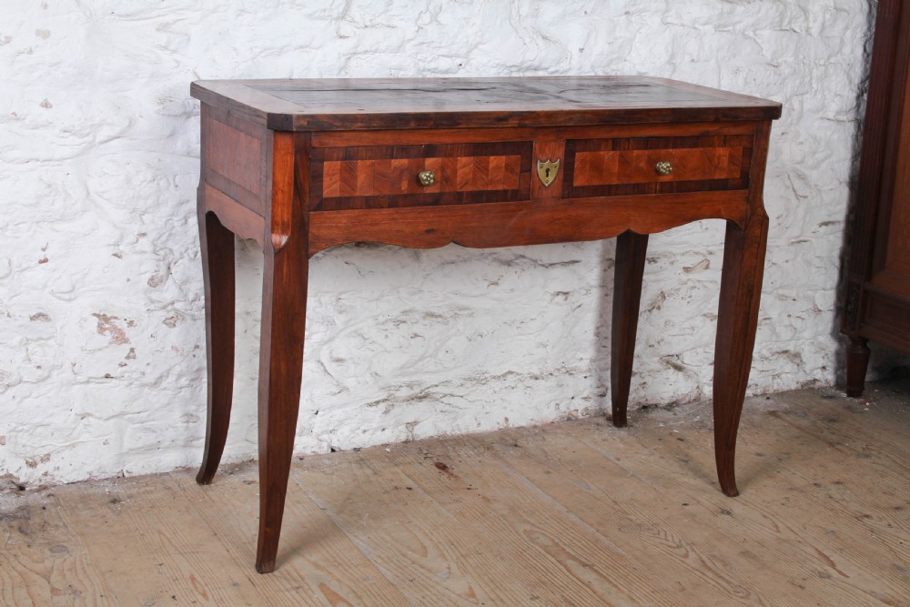 An antique warm brown wooden writing table featuring geometric parquetry inlay on two drawers, slender cabriole legs, and a central brass escutcheon keyhole.