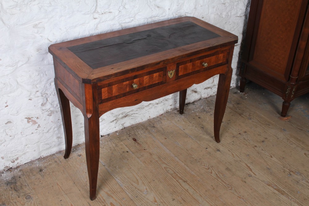 An antique warm brown wooden writing table featuring geometric parquetry inlay on two drawers, slender cabriole legs, and a central brass escutcheon keyhole. View II