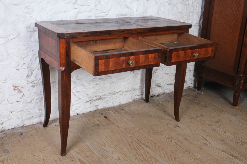 An antique warm brown wooden writing table featuring geometric parquetry inlay on two drawers, slender cabriole legs, and a central brass escutcheon keyhole. View V