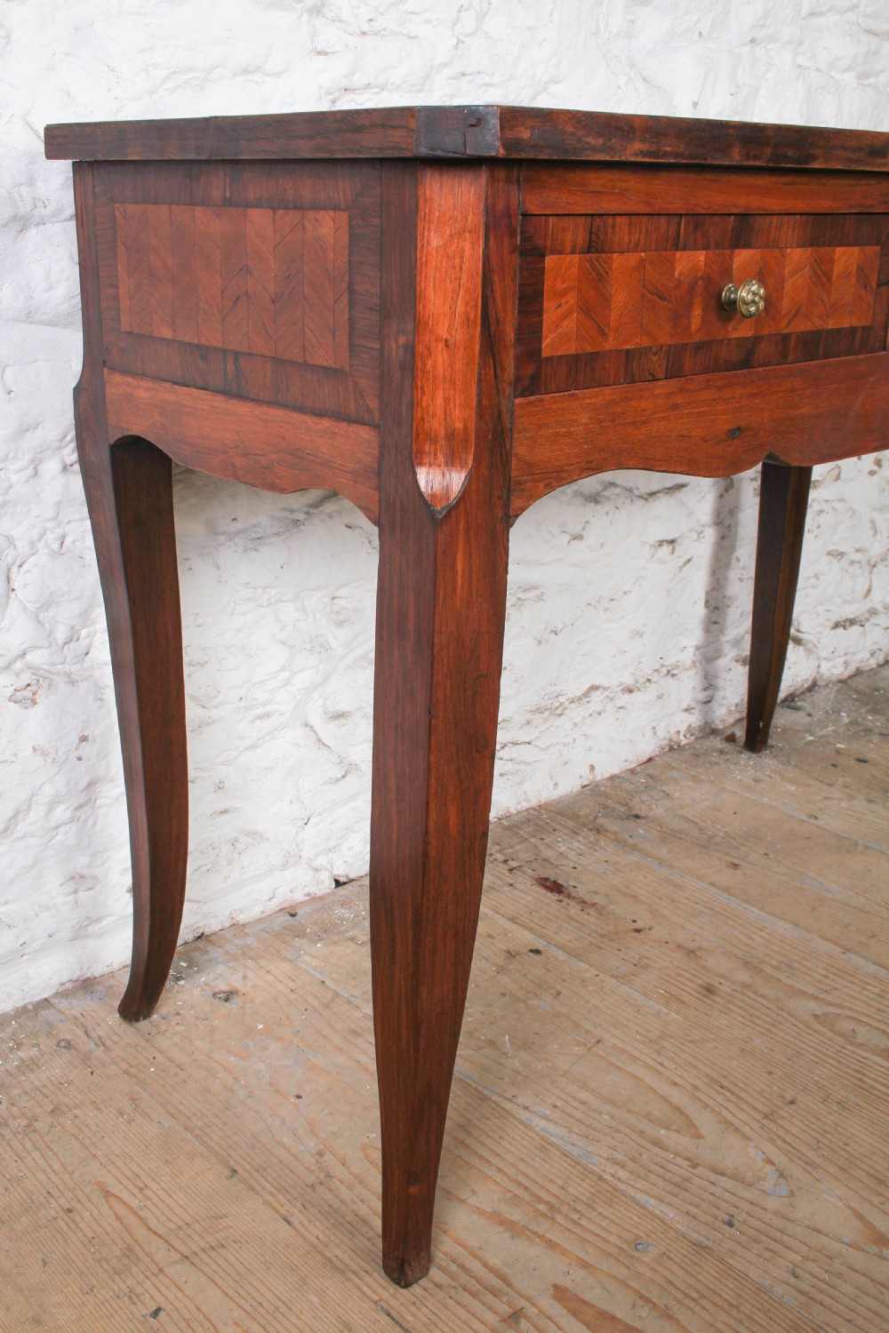 An antique warm brown wooden writing table featuring geometric parquetry inlay on two drawers, slender cabriole legs, and a central brass escutcheon keyhole. View VI