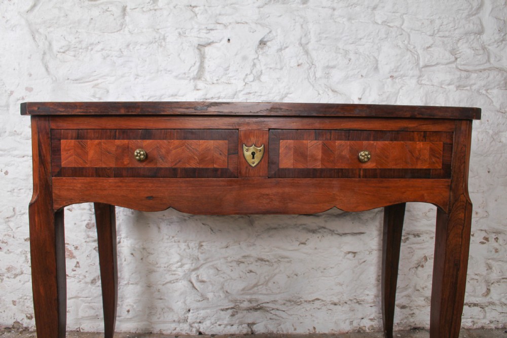An antique warm brown wooden writing table featuring geometric parquetry inlay on two drawers, slender cabriole legs, and a central brass escutcheon keyhole. View VII