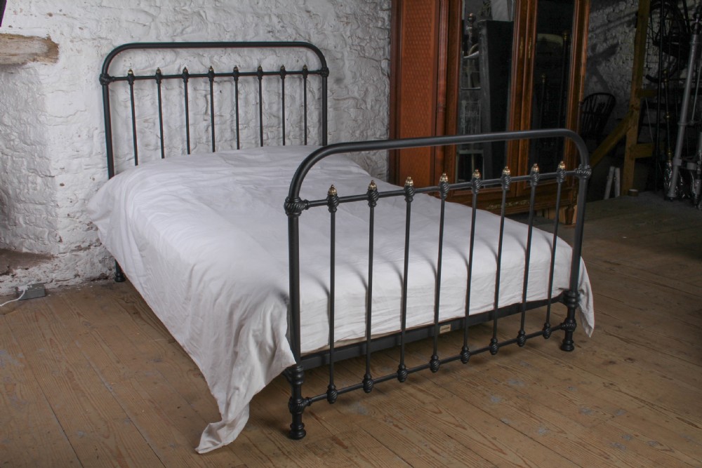 A black iron double bed frame with vertical upright spindles and decorative brass finial accents.