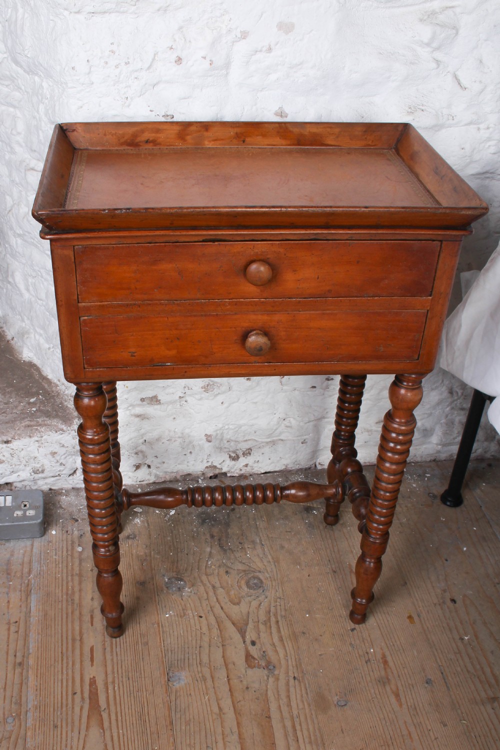 An antique warm brown wooden side table featuring bobbin-turned legs, a tray top, two drawers with round wooden knobs, and a turned stretcher. View VI