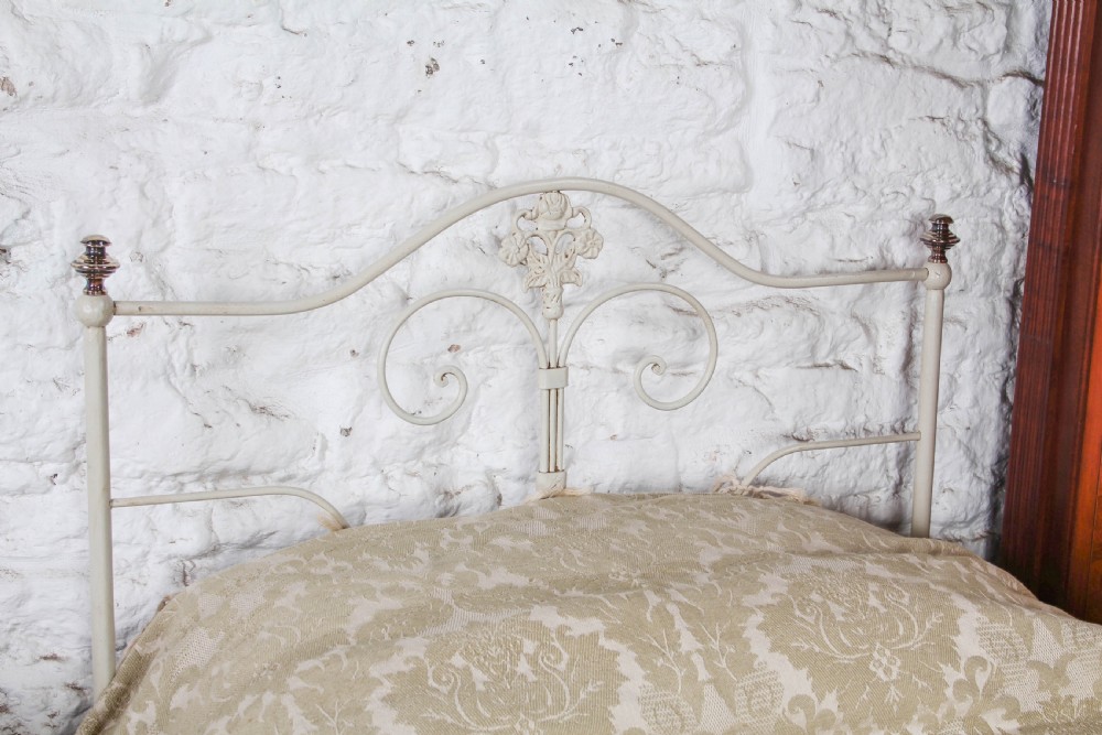 A pair of cream-painted antique Portuguese iron single beds featuring decorative scrolled headboards and low-profile foot ends. View III
