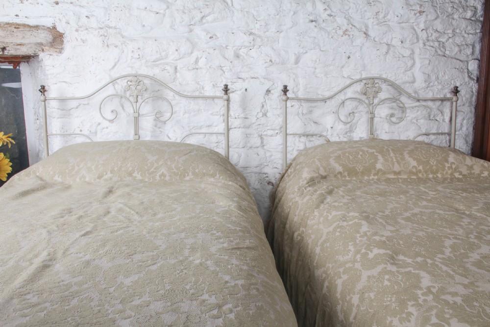 A pair of cream-painted antique Portuguese iron single beds featuring decorative scrolled headboards and low-profile foot ends. View VII