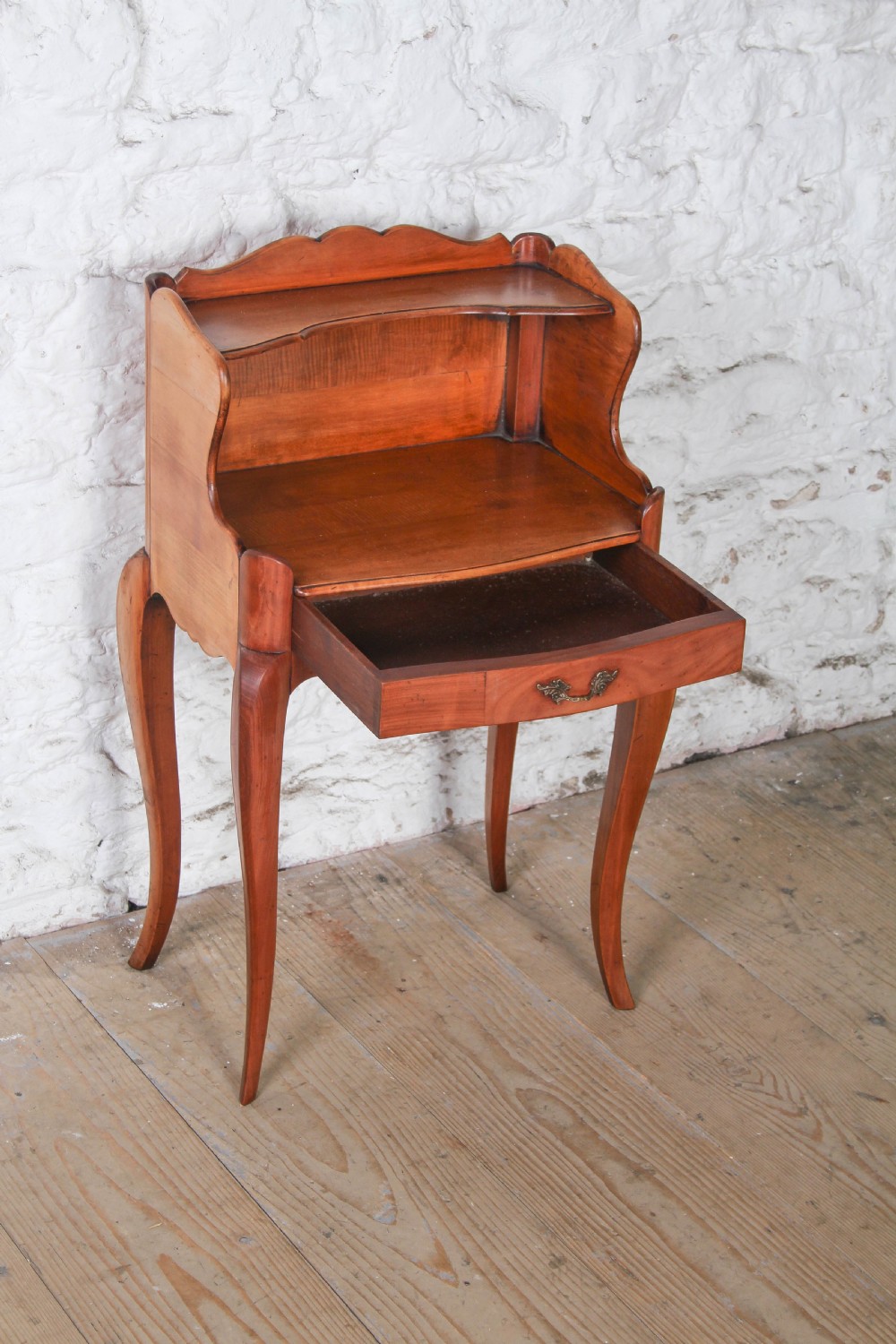 A French Louis XV style cherrywood bedside table featuring slender cabriole legs, a single drawer with a brass handle, and an upper gallery shelf. View II