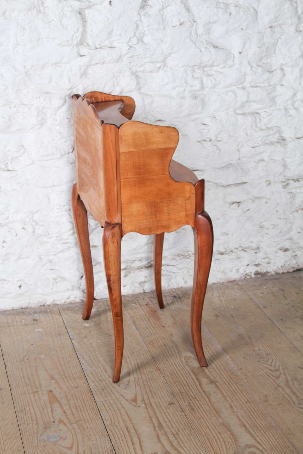 A French Louis XV style cherrywood bedside table featuring slender cabriole legs, a single drawer with a brass handle, and an upper gallery shelf. View III