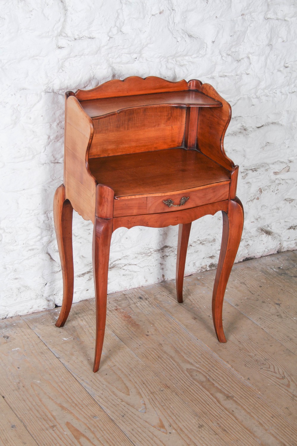 A French Louis XV style cherrywood bedside table featuring slender cabriole legs, a single drawer with a brass handle, and an upper gallery shelf. View IV