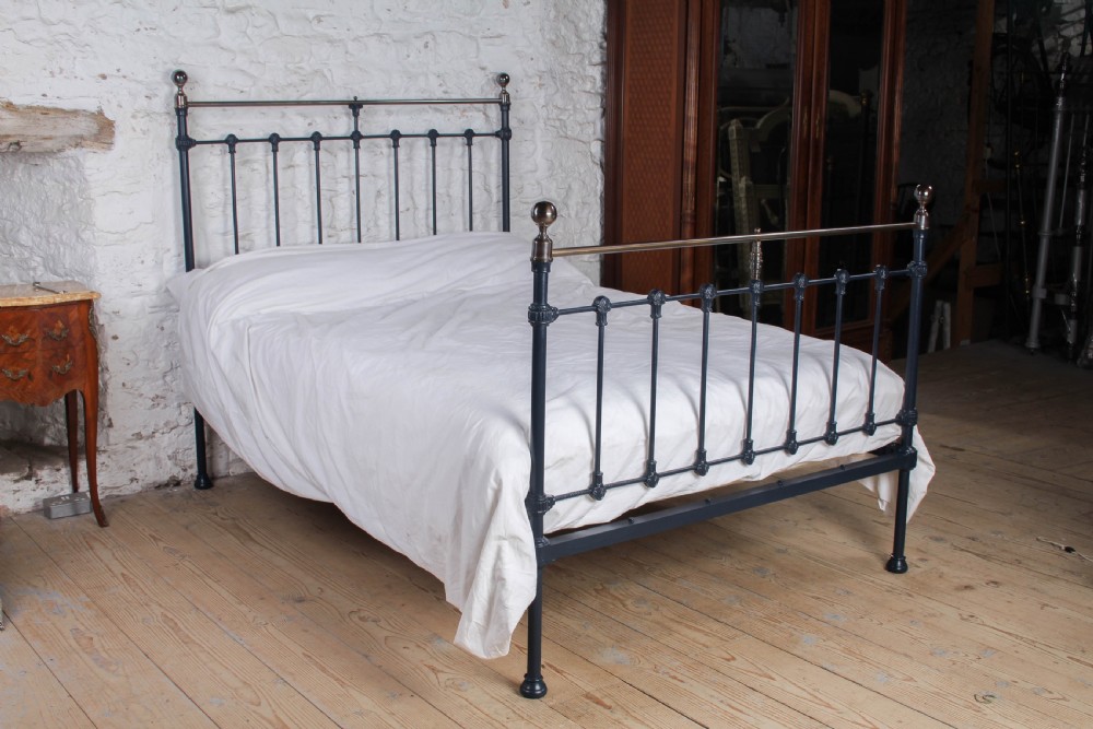 An Edwardian iron and brass double bedstead featuring dark vertical spindles, decorative cast collars, and polished brass top rails with brass finials.