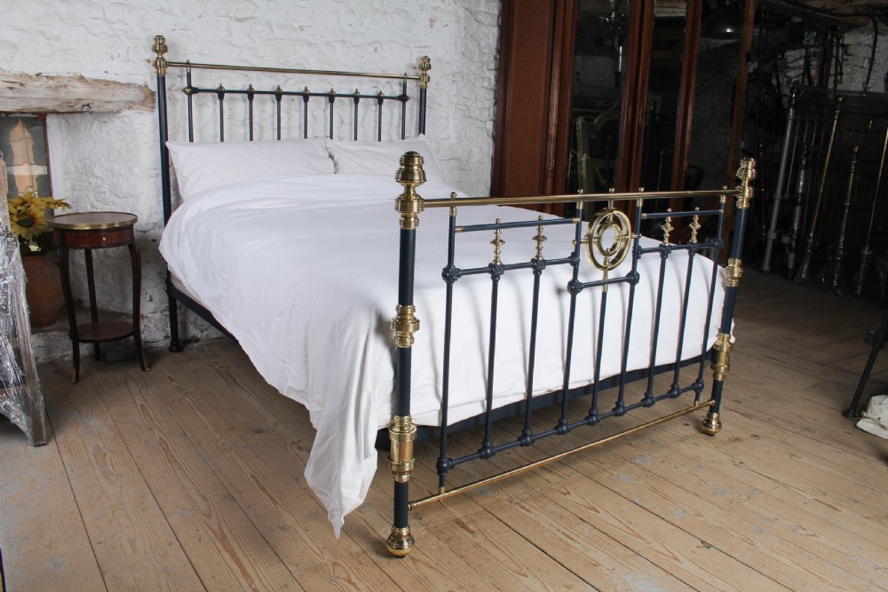 A Victorian king size bedstead crafted from black iron with polished brass rails, finials, and a central circular brass motif.