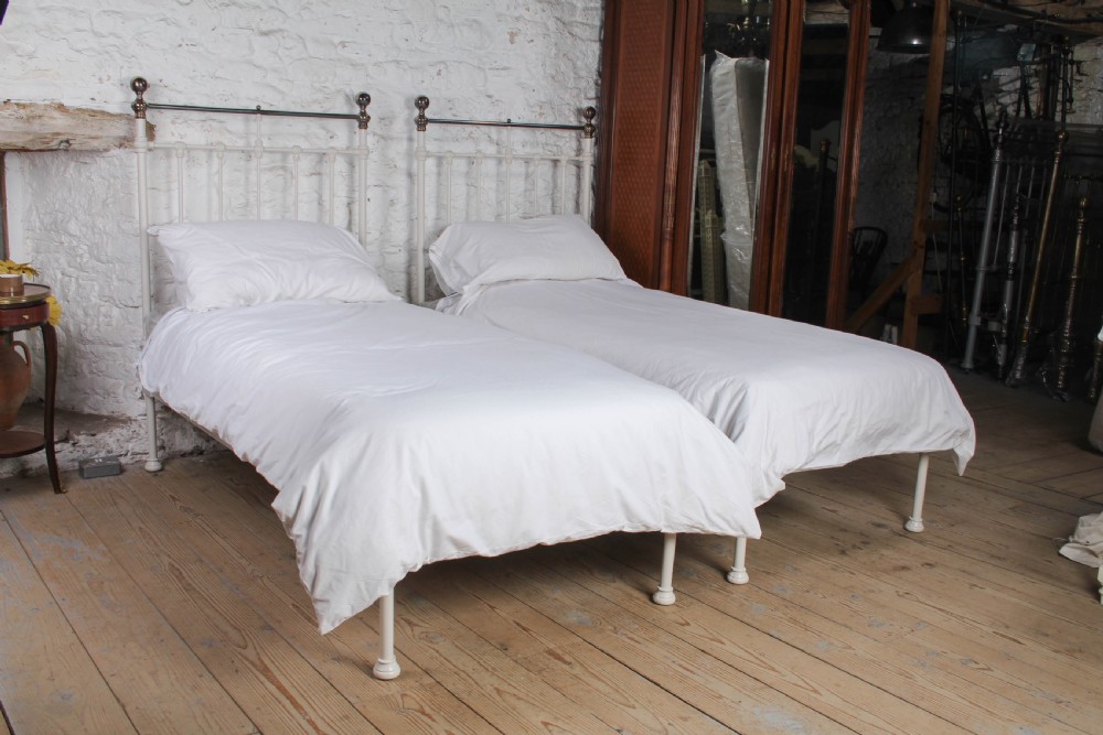 A pair of white painted Victorian single bed frames with vertical iron spindles and brass top rails.