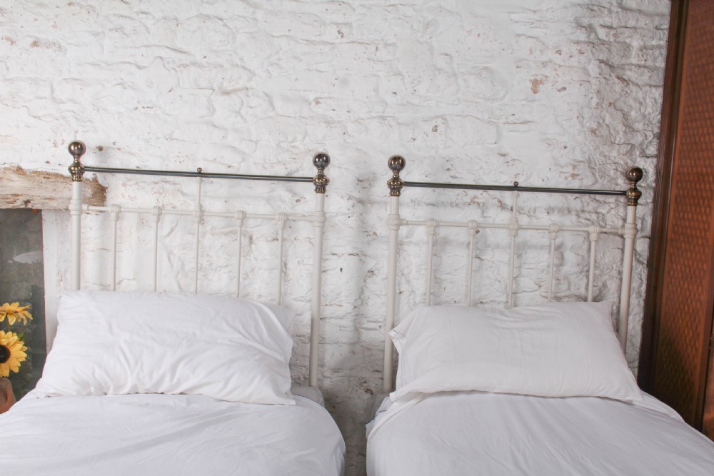 A pair of white painted Victorian single bed frames with vertical iron spindles and brass top rails. View II