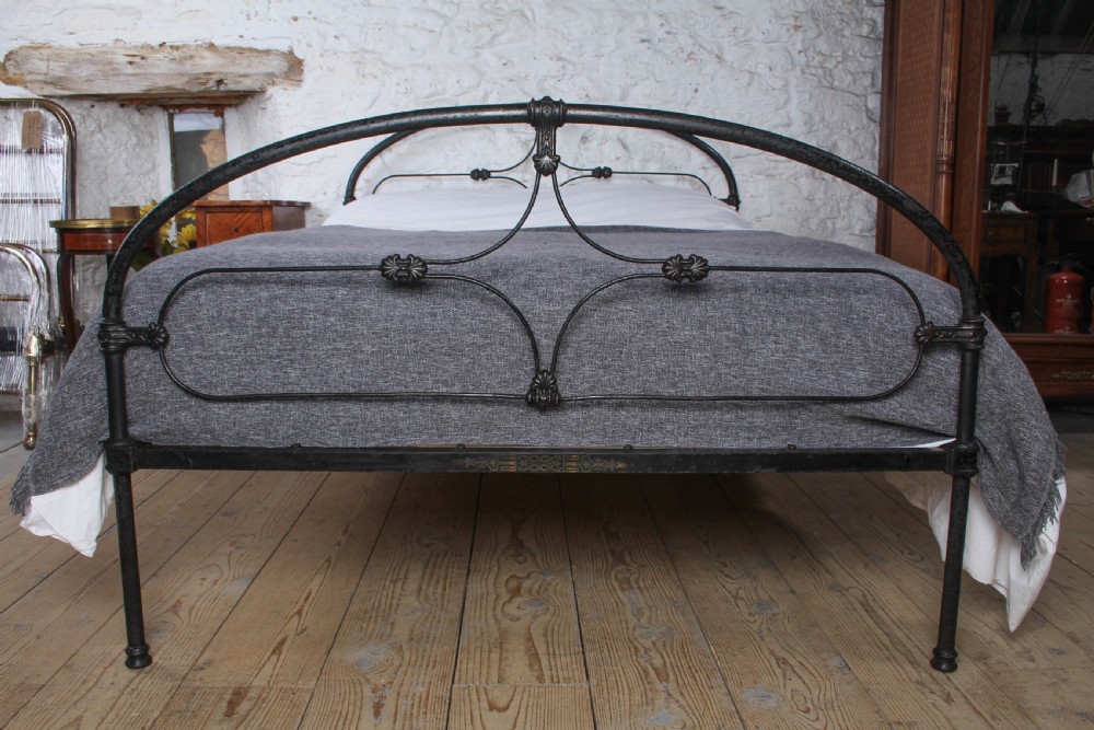 An antique dark wrought iron double bed frame featuring arched headboard and footboard rails with decorative cast rosettes. View II