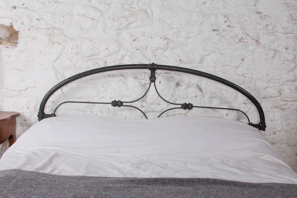 An antique dark wrought iron double bed frame featuring arched headboard and footboard rails with decorative cast rosettes. View V