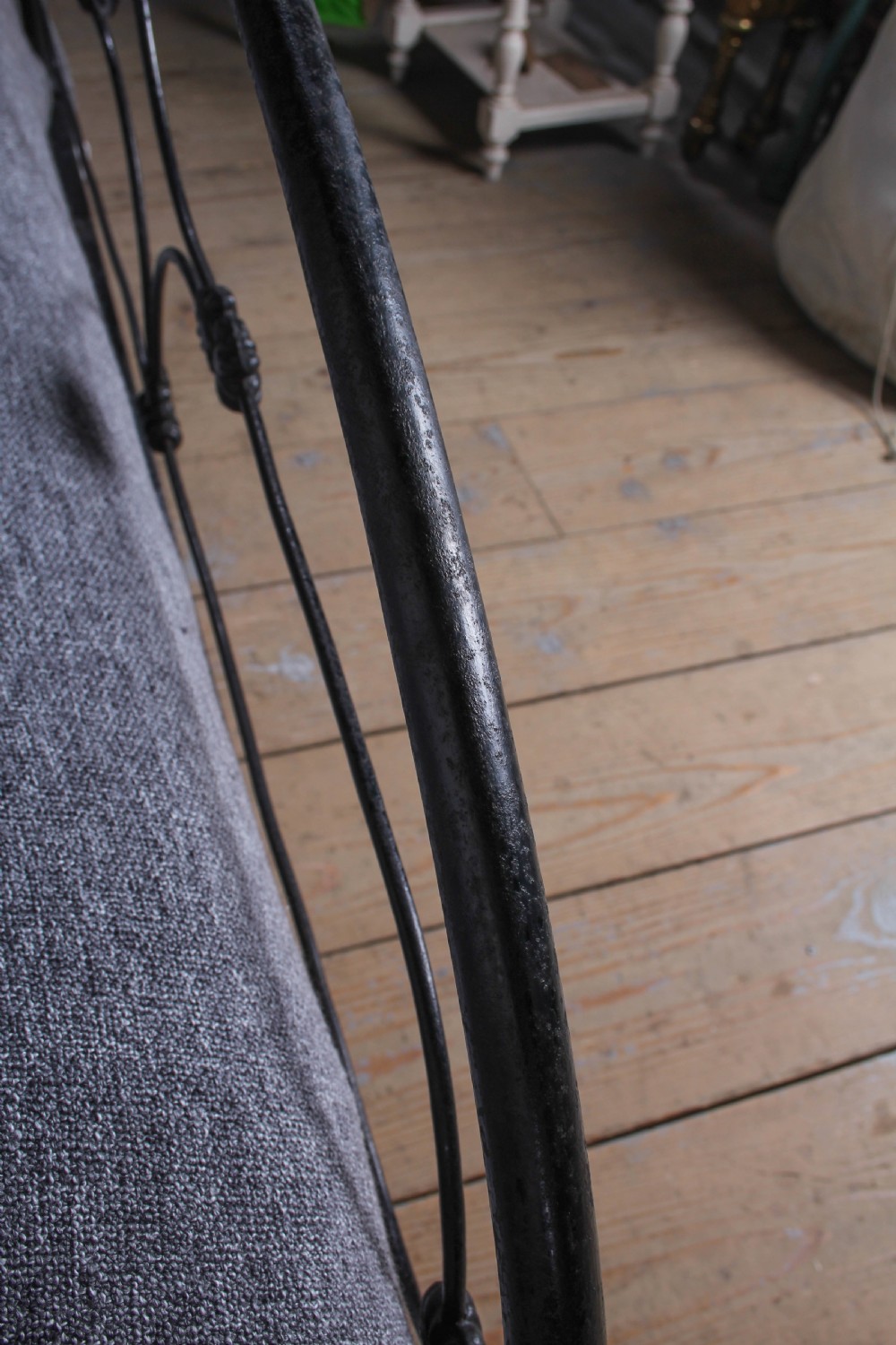 An antique dark wrought iron double bed frame featuring arched headboard and footboard rails with decorative cast rosettes. View VI