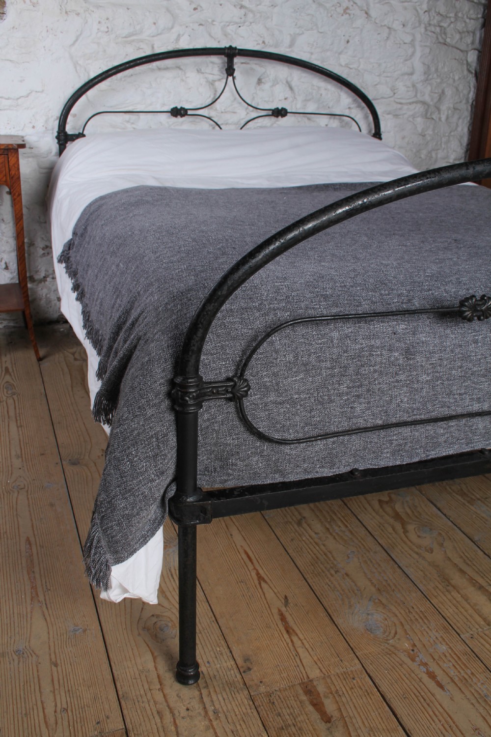 An antique dark wrought iron double bed frame featuring arched headboard and footboard rails with decorative cast rosettes. View VIII