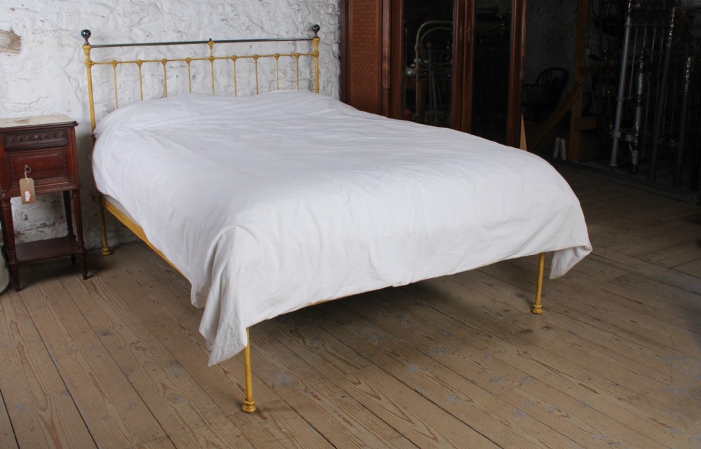 A king-size yellow painted iron bedstead featuring a vertical spindle headboard with a brass top rail and no footboard.