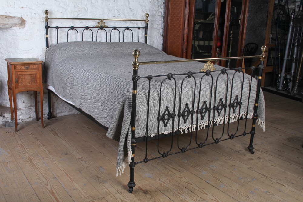 A Victorian five-foot king-size bedstead featuring a black japanned cast iron frame with vertical arched spindles, central diamond motifs, and brass top rails with brass finials.
