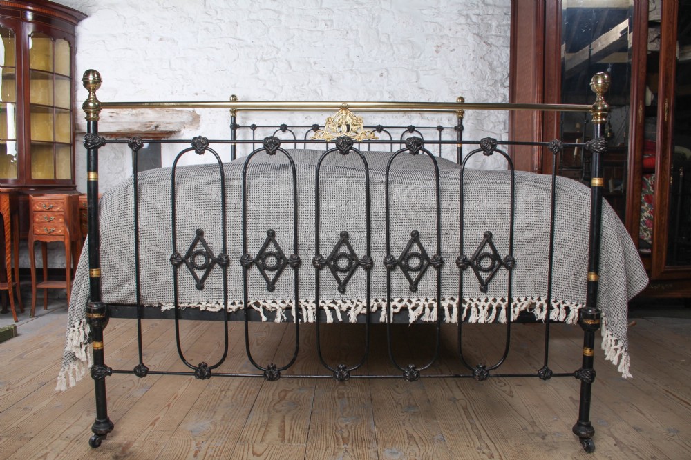 A Victorian five-foot king-size bedstead featuring a black japanned cast iron frame with vertical arched spindles, central diamond motifs, and brass top rails with brass finials. View II