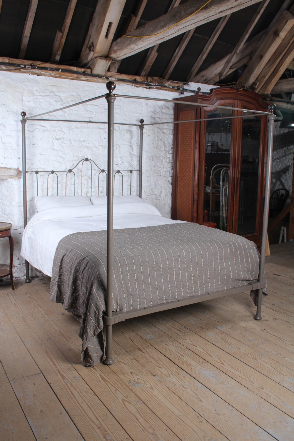 A low height king size metal four poster bed frame with slender corner posts, brass finials, and an arched headboard with vertical iron spindles.