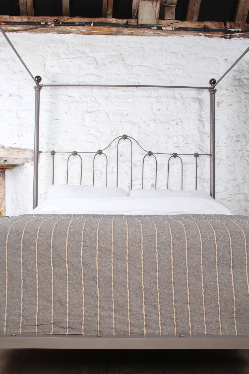 A low height king size metal four poster bed frame with slender corner posts, brass finials, and an arched headboard with vertical iron spindles. View VII
