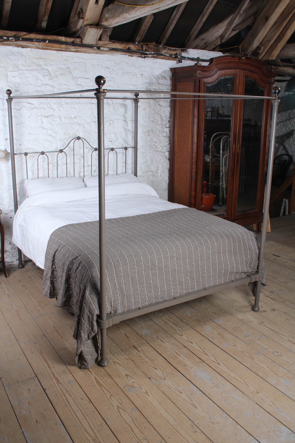 A low height king size metal four poster bed frame with slender corner posts, brass finials, and an arched headboard with vertical iron spindles. View VIII