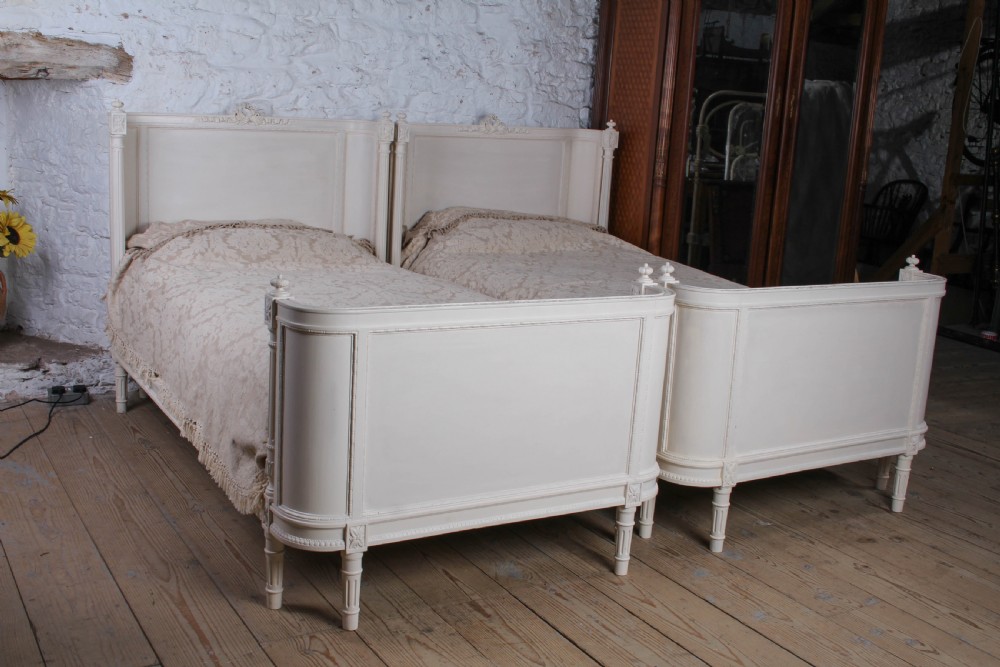 A pair of off-white painted French corbeille single bed frames featuring curved footboards, carved details, and fluted legs. View II