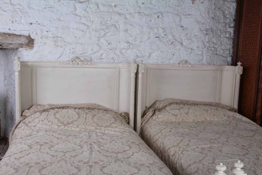 A pair of off-white painted French corbeille single bed frames featuring curved footboards, carved details, and fluted legs. View IV
