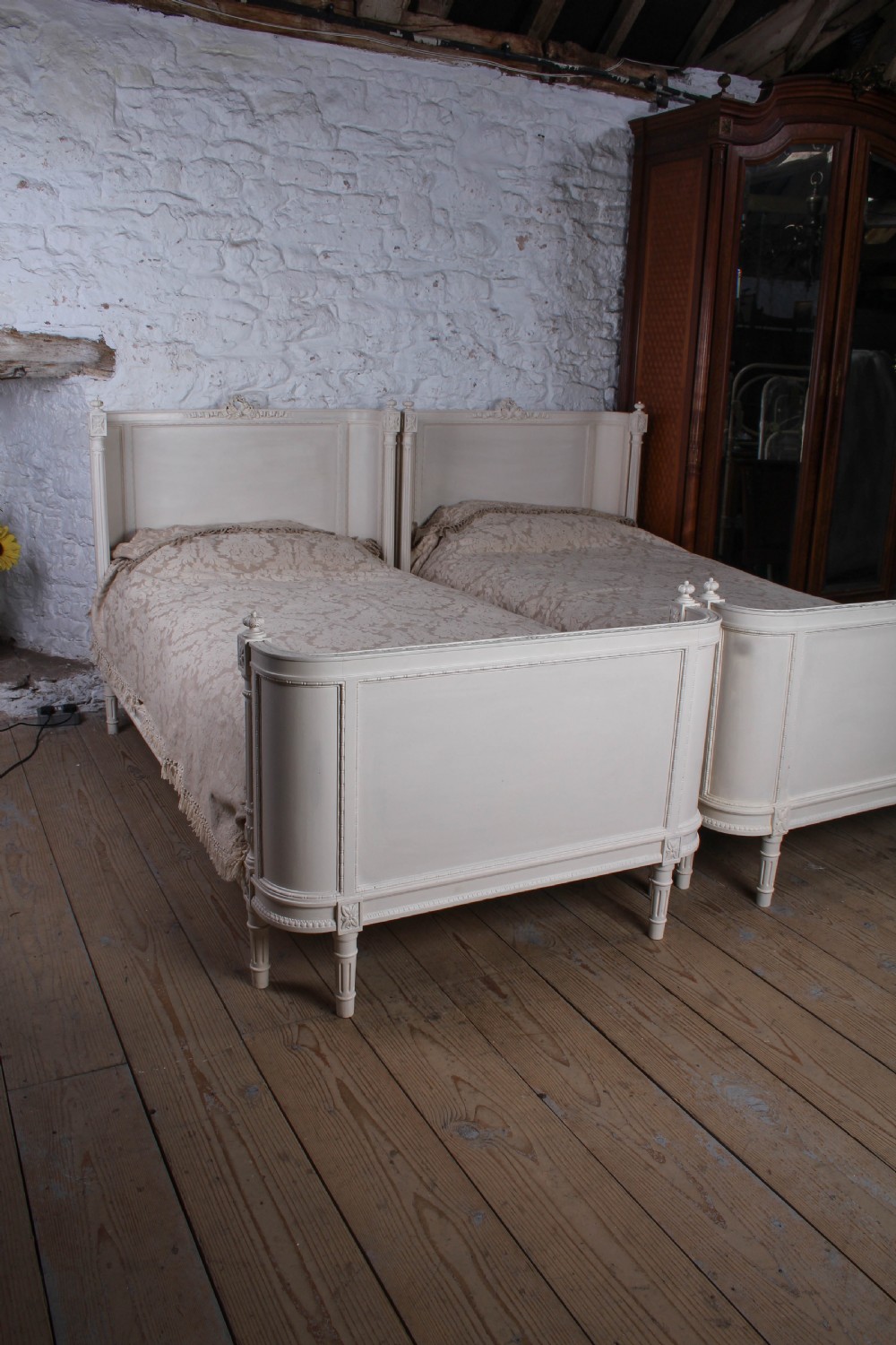 A pair of off-white painted French corbeille single bed frames featuring curved footboards, carved details, and fluted legs. View V