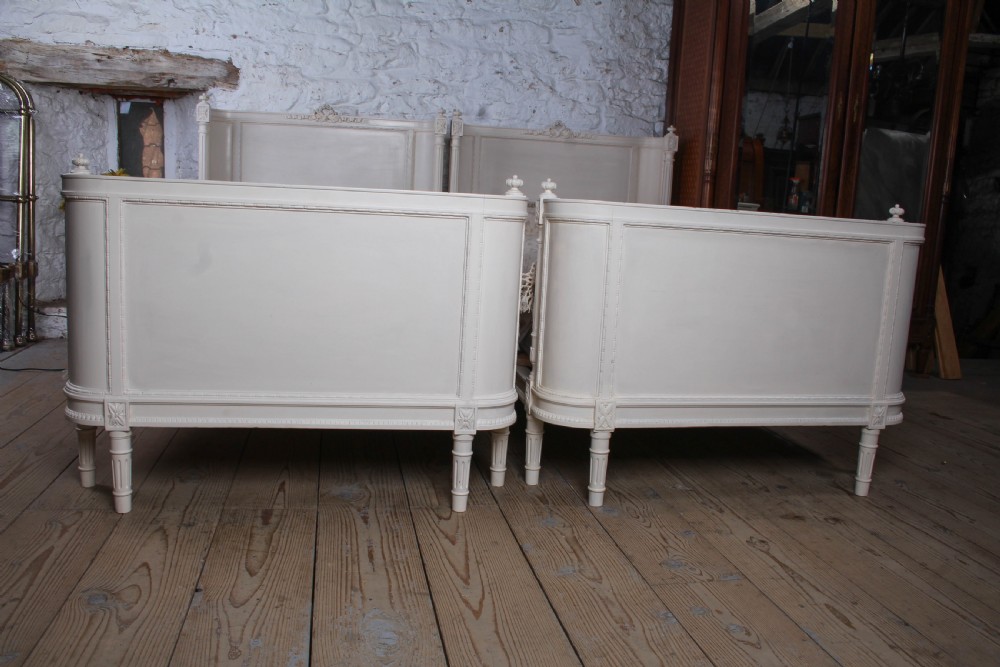 A pair of off-white painted French corbeille single bed frames featuring curved footboards, carved details, and fluted legs. View VI