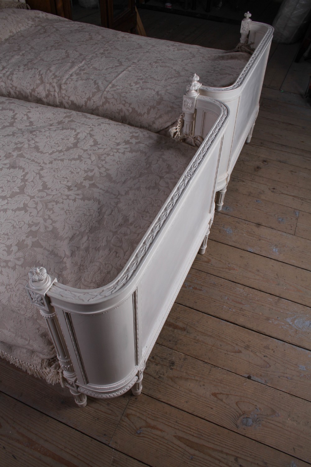 A pair of off-white painted French corbeille single bed frames featuring curved footboards, carved details, and fluted legs. View VII