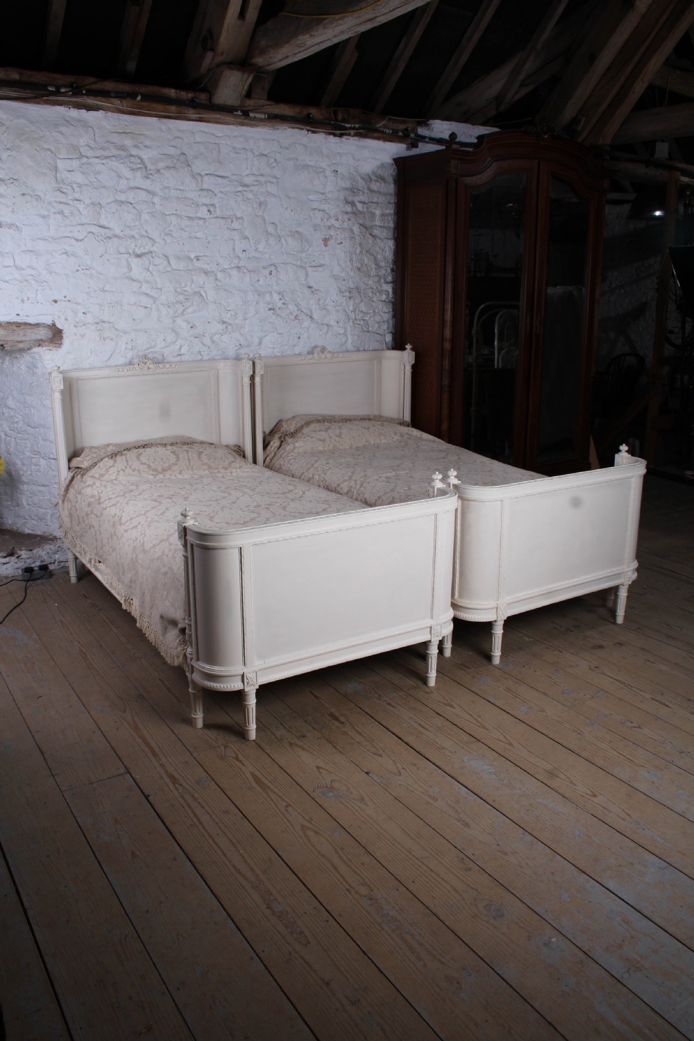 A pair of off-white painted French corbeille single bed frames featuring curved footboards, carved details, and fluted legs. View IX
