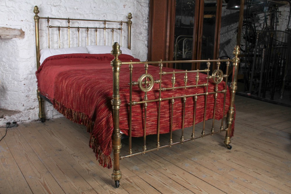 A Victorian brass king-size bed frame featuring turned upright posts, urn finials, vertical decorative spindles, circular roundels, and original castors.
