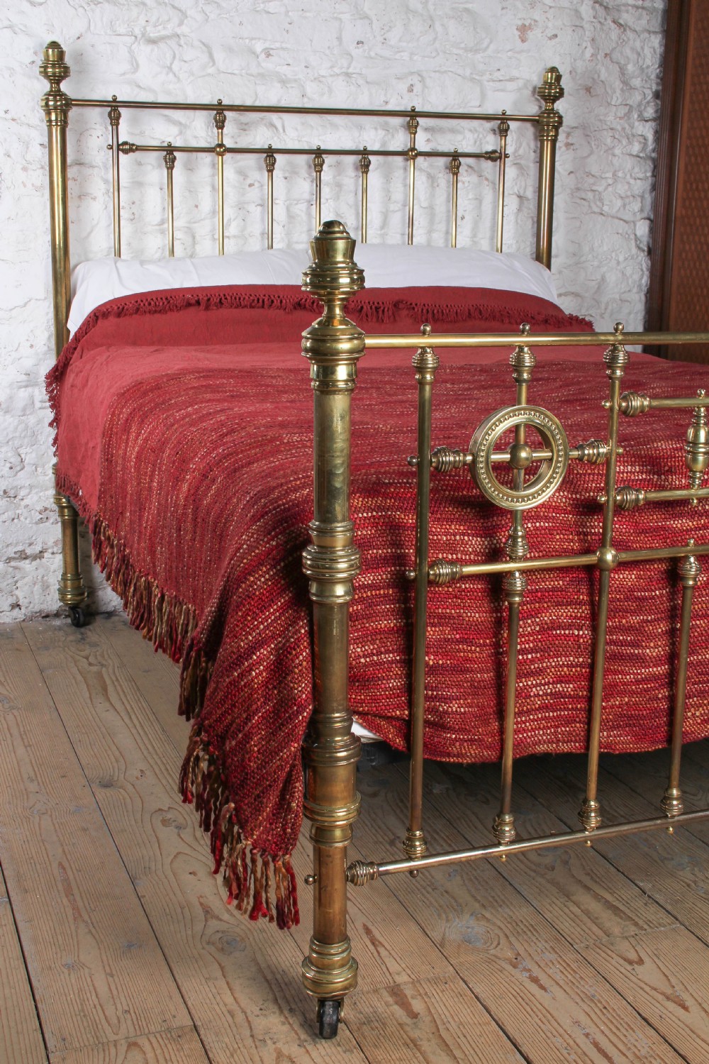 A Victorian brass king-size bed frame featuring turned upright posts, urn finials, vertical decorative spindles, circular roundels, and original castors. View II