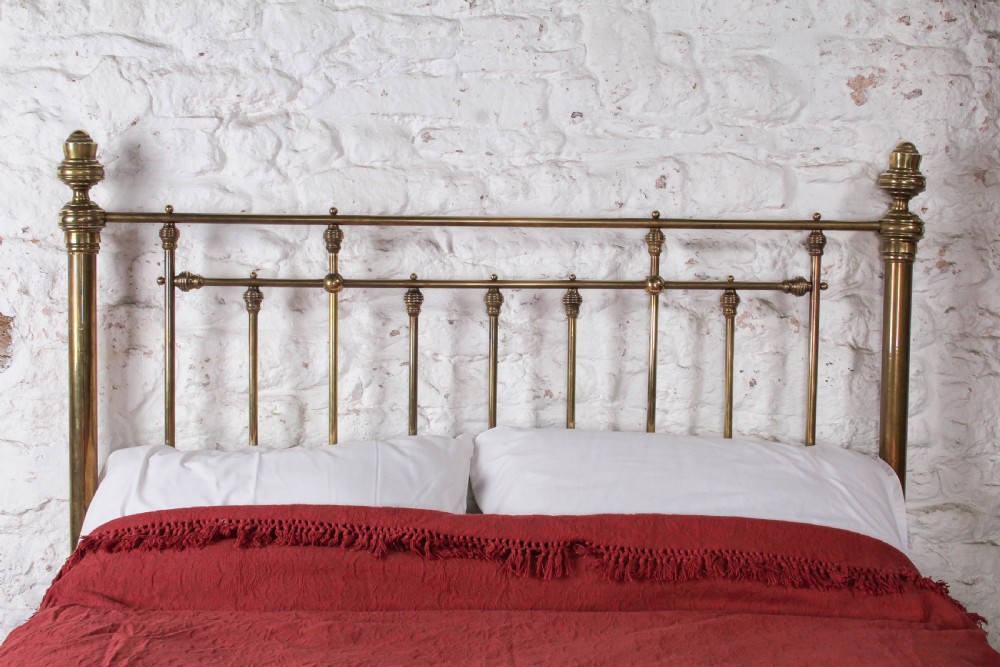 A Victorian brass king-size bed frame featuring turned upright posts, urn finials, vertical decorative spindles, circular roundels, and original castors. View III