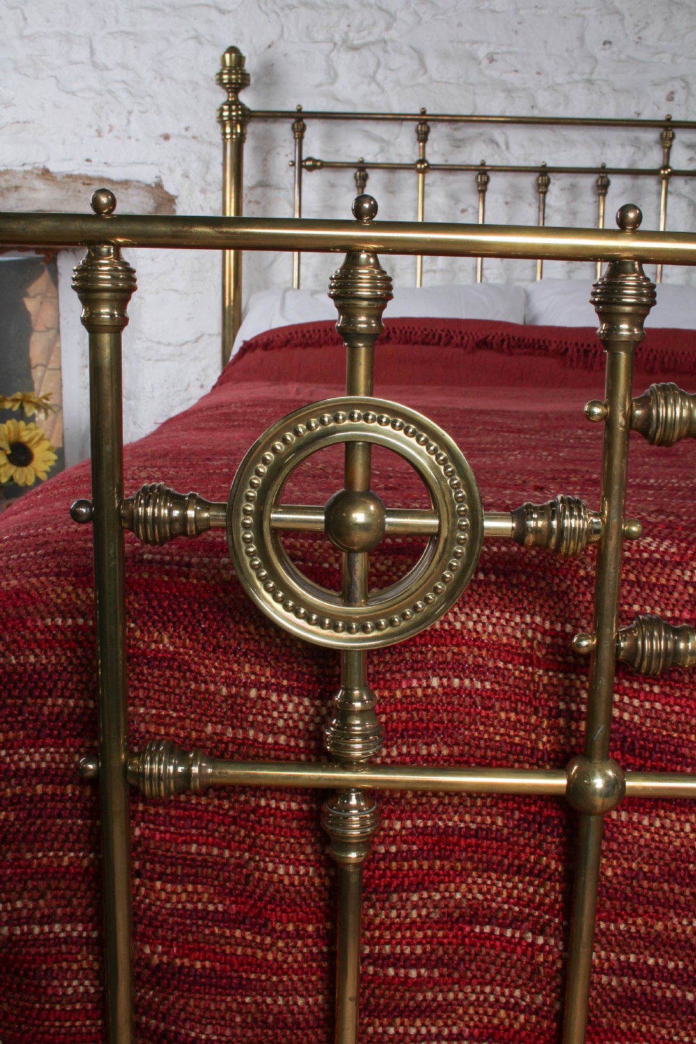 A Victorian brass king-size bed frame featuring turned upright posts, urn finials, vertical decorative spindles, circular roundels, and original castors. View VI