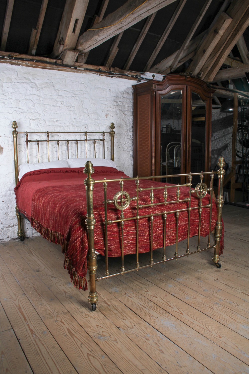 A Victorian brass king-size bed frame featuring turned upright posts, urn finials, vertical decorative spindles, circular roundels, and original castors. View IX