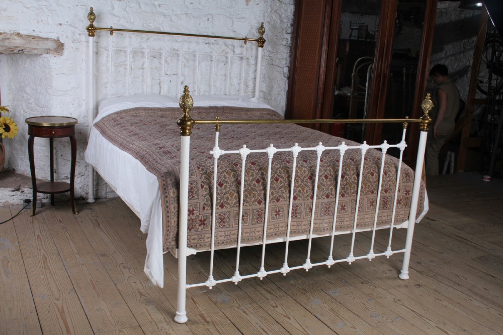 A Victorian white painted iron bedstead featuring brass top rails and brass urn finials on the headboard and footboard.