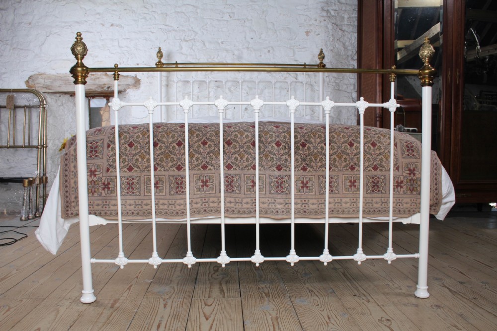 A Victorian white painted iron bedstead featuring brass top rails and brass urn finials on the headboard and footboard. View II