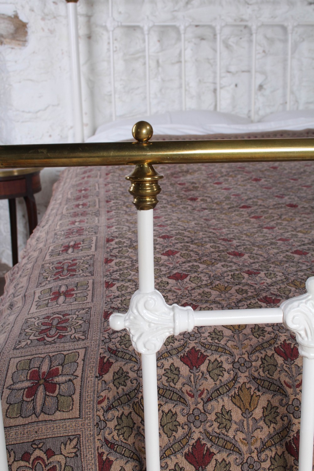 A Victorian white painted iron bedstead featuring brass top rails and brass urn finials on the headboard and footboard. View V