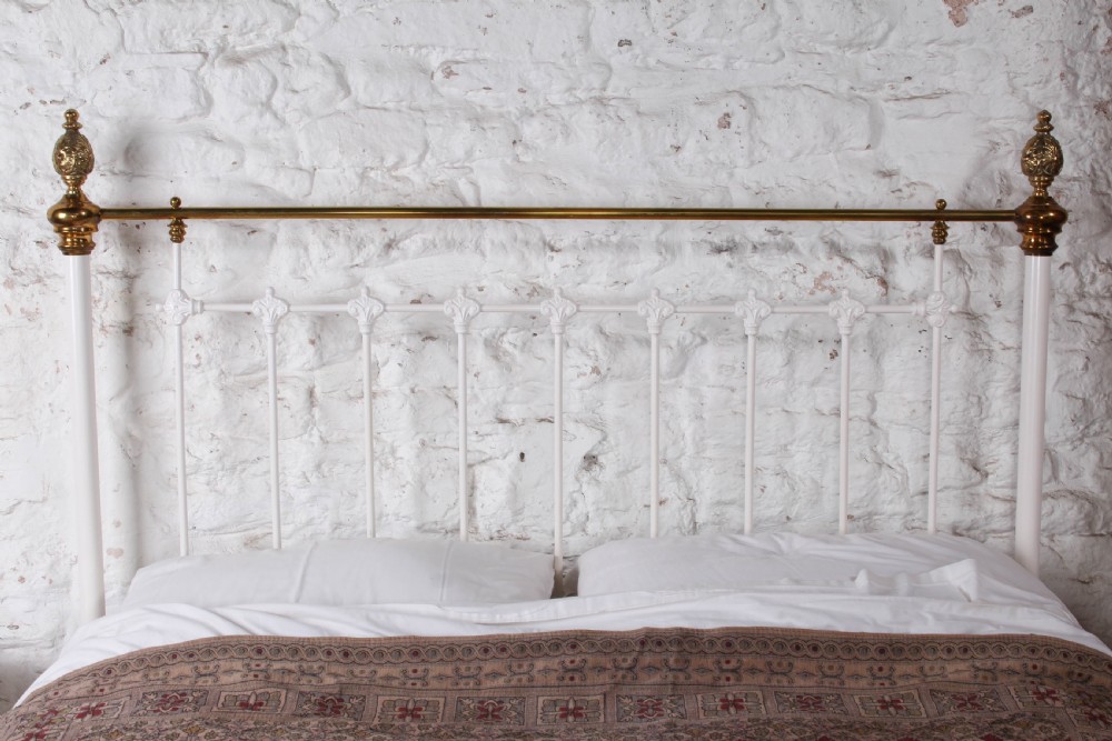 A Victorian white painted iron bedstead featuring brass top rails and brass urn finials on the headboard and footboard. View VII