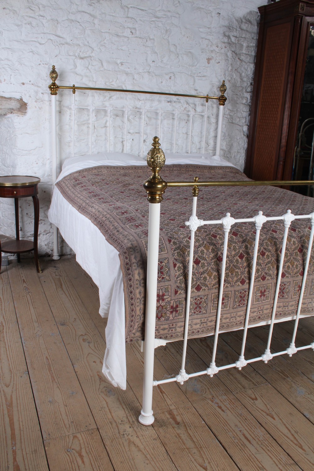 A Victorian white painted iron bedstead featuring brass top rails and brass urn finials on the headboard and footboard. View VIII